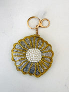 A handmade beaded flower-shaped keychain with a gold-tone clasp, featuring a white beaded center and gold and silver beaded petals, set against a plain off-white background.