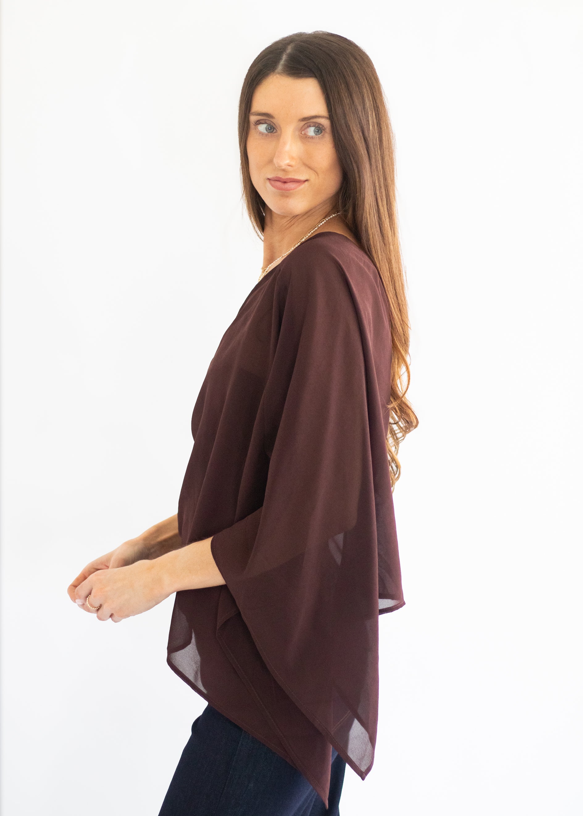 A woman wearing a dark brown, semi-sheer draped top with wide three-quarter sleeves, shown from a side-back angle against a plain white background.