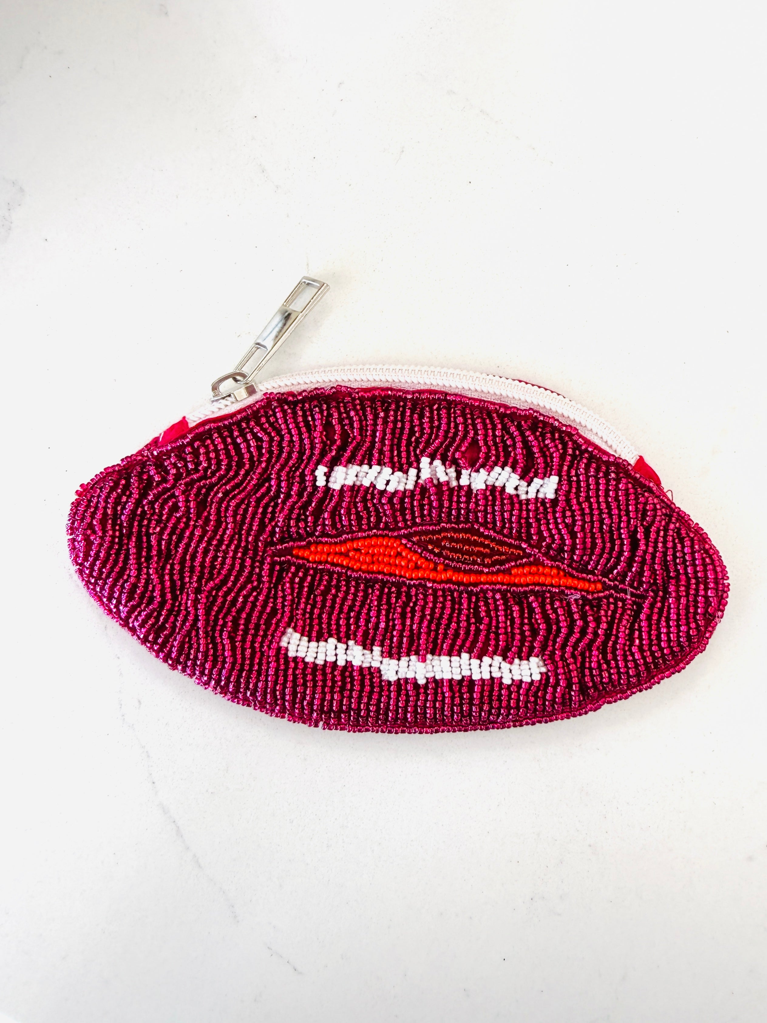 A small zippered pouch shaped like a pair of lips, covered in dark magenta and pink beaded texture with white bead details for the teeth and a red bead accent for the lips, shown on a white background.