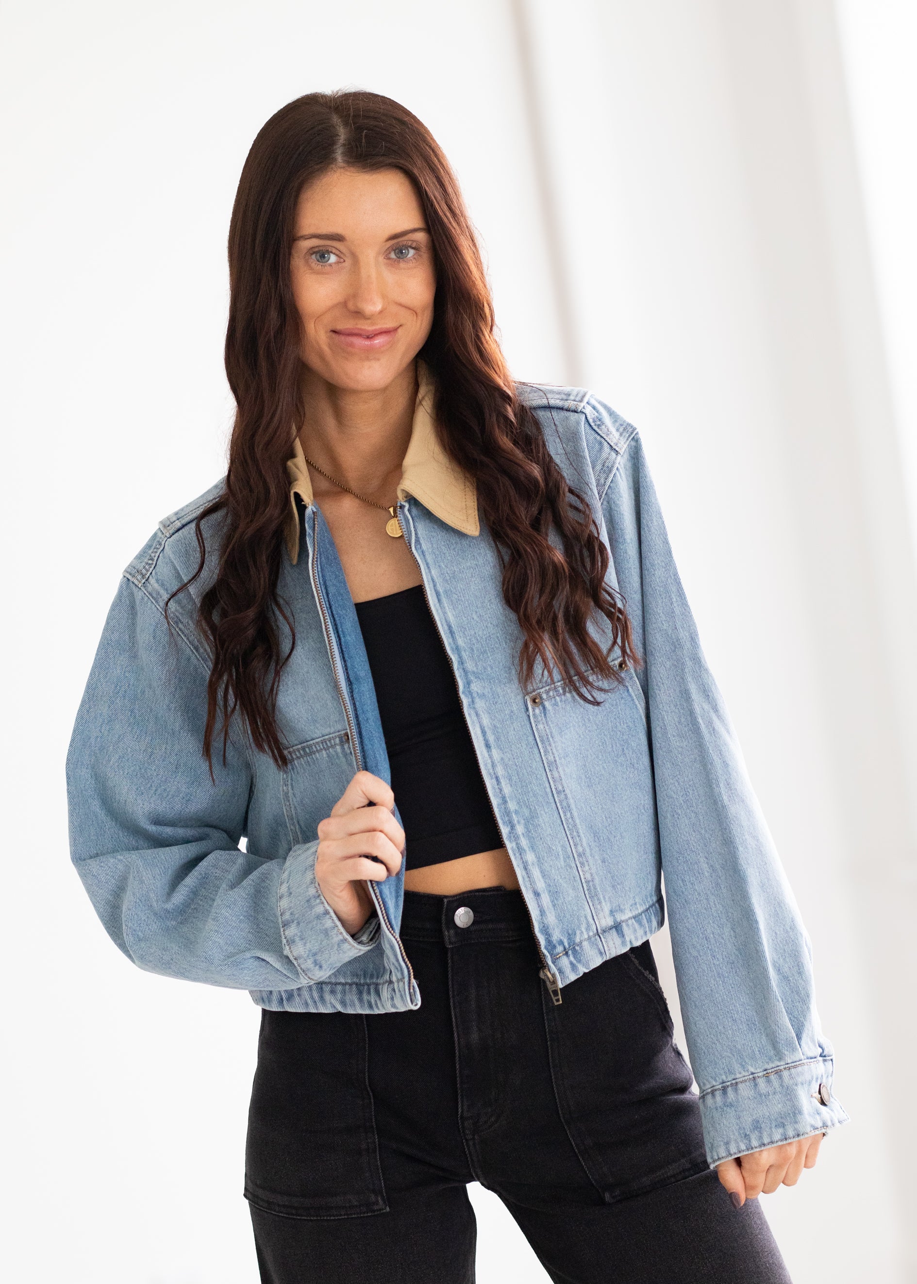 Woman wearing a light blue denim jacket over a black top and pants on a white background