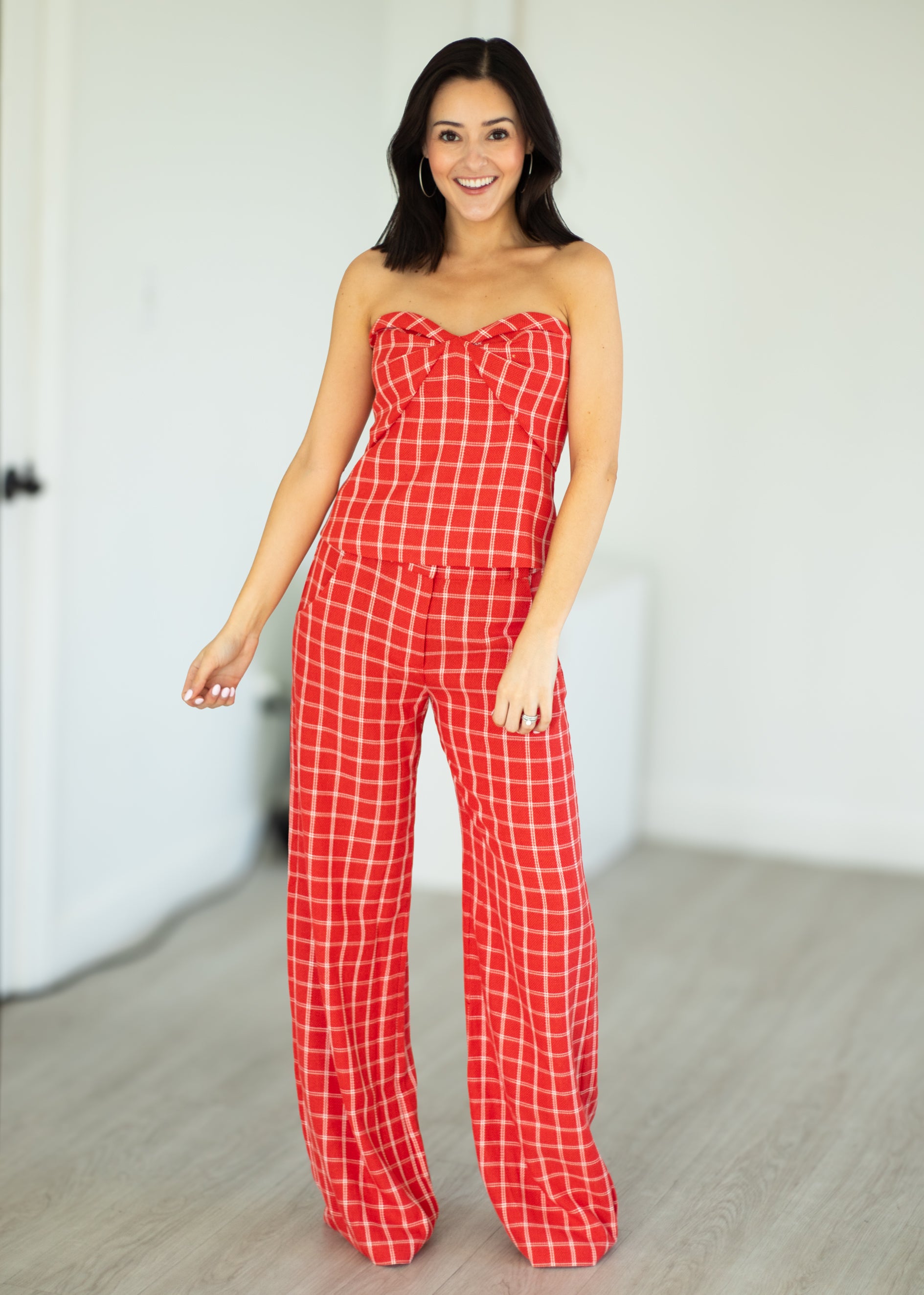 Woman wearing a red checkered strapless jumpsuit against a plain background