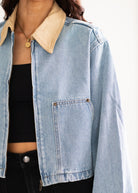 Light blue denim jacket with beige collar worn by a person on a white background
