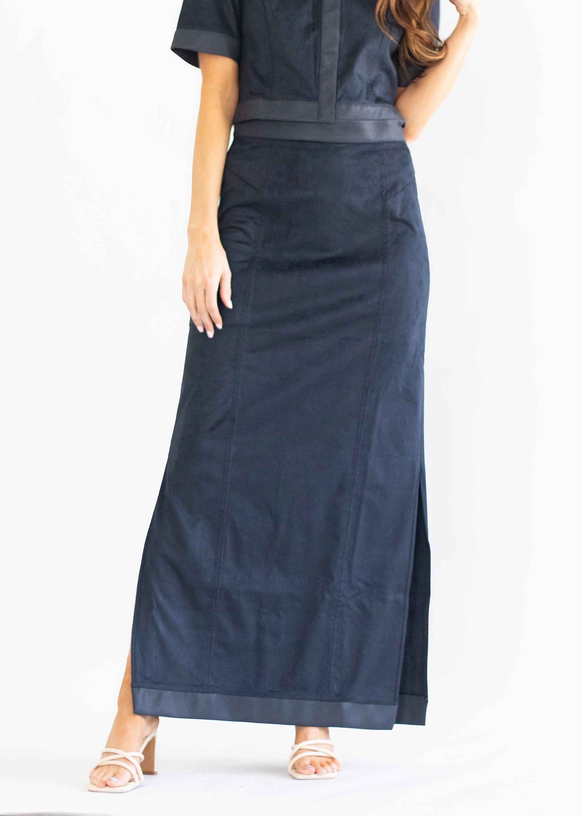 A woman modeling a long navy blue skirt with a matching top, shown from the waist down against a plain white studio background.