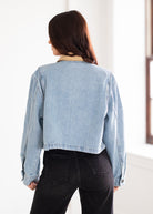 Person wearing a light blue denim jacket and black pants in a bright room.