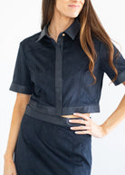 A woman wearing a dark navy blue short-sleeve collared shirt with contrasting smooth trim and a matching dark skirt, shown against a plain white background.