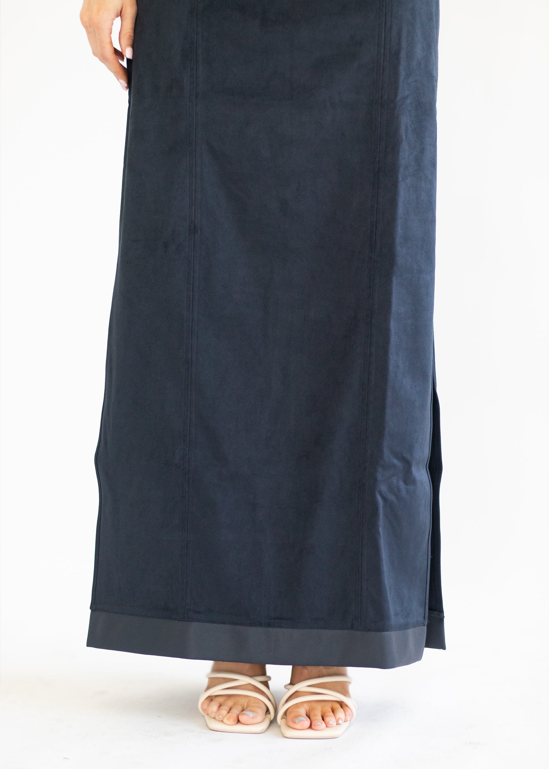A navy blue maxi skirt with side slits, shown on a model from the waist down wearing beige strappy sandals against a white studio background.