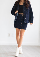 Person wearing a dark denim jacket, skirt, and white boots on a plain background