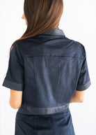 A woman shown from the back wearing a dark navy blue short-sleeve cropped jacket with contrasting dark gray trim on the collar, cuffs, and hem, against a plain white background.