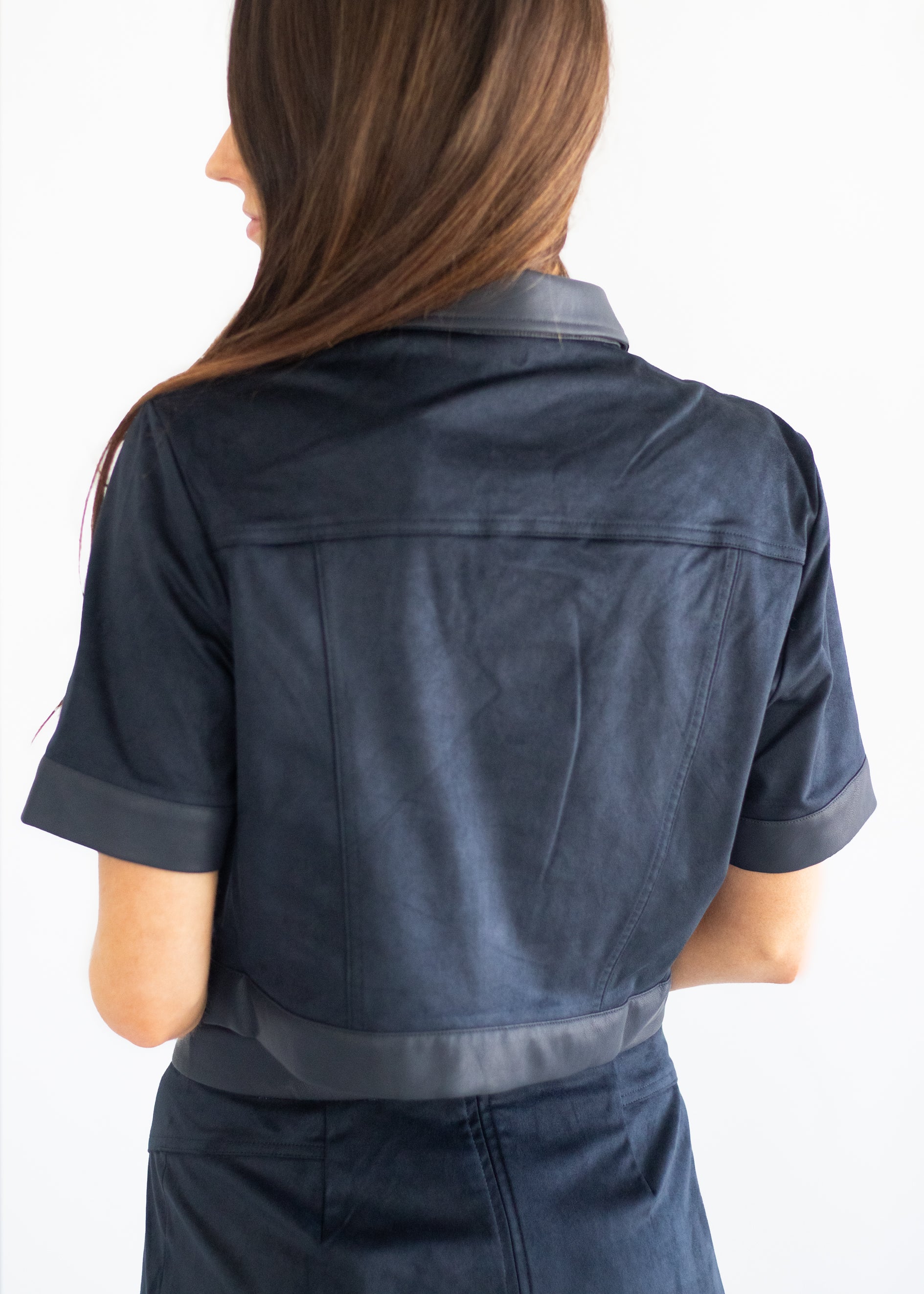 A woman shown from the back wearing a dark navy blue short-sleeve cropped jacket with contrasting dark gray trim on the collar, cuffs, and hem, against a plain white background.