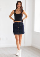 Woman wearing a black tank top and denim skirt with white boots in a minimalistic setting