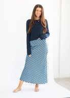 A woman modeling a dark navy blue ribbed knit cardigan and a blue and white striped midi skirt, standing against a clean white studio backdrop.