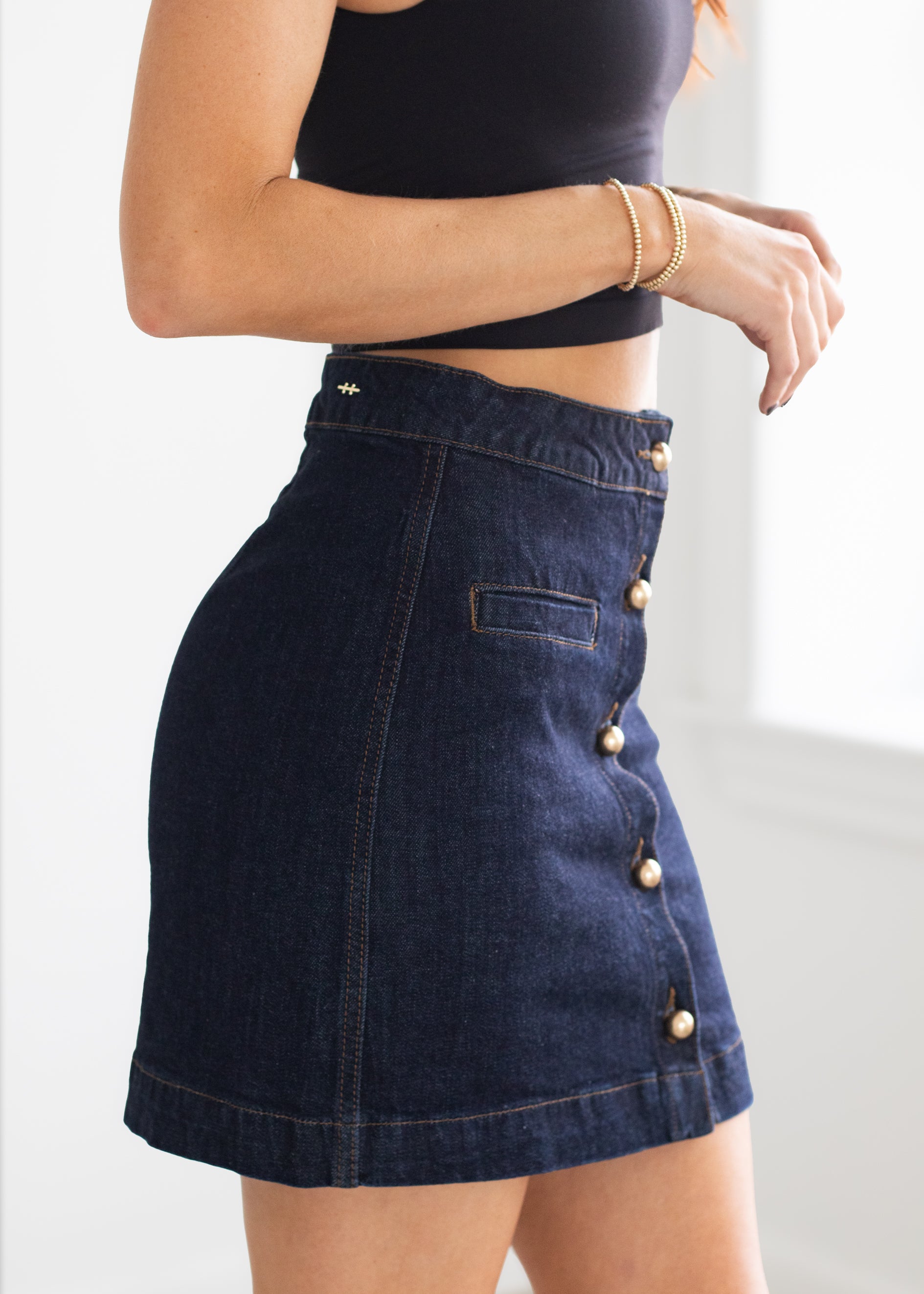 Person wearing a dark denim skirt with button details on a white background