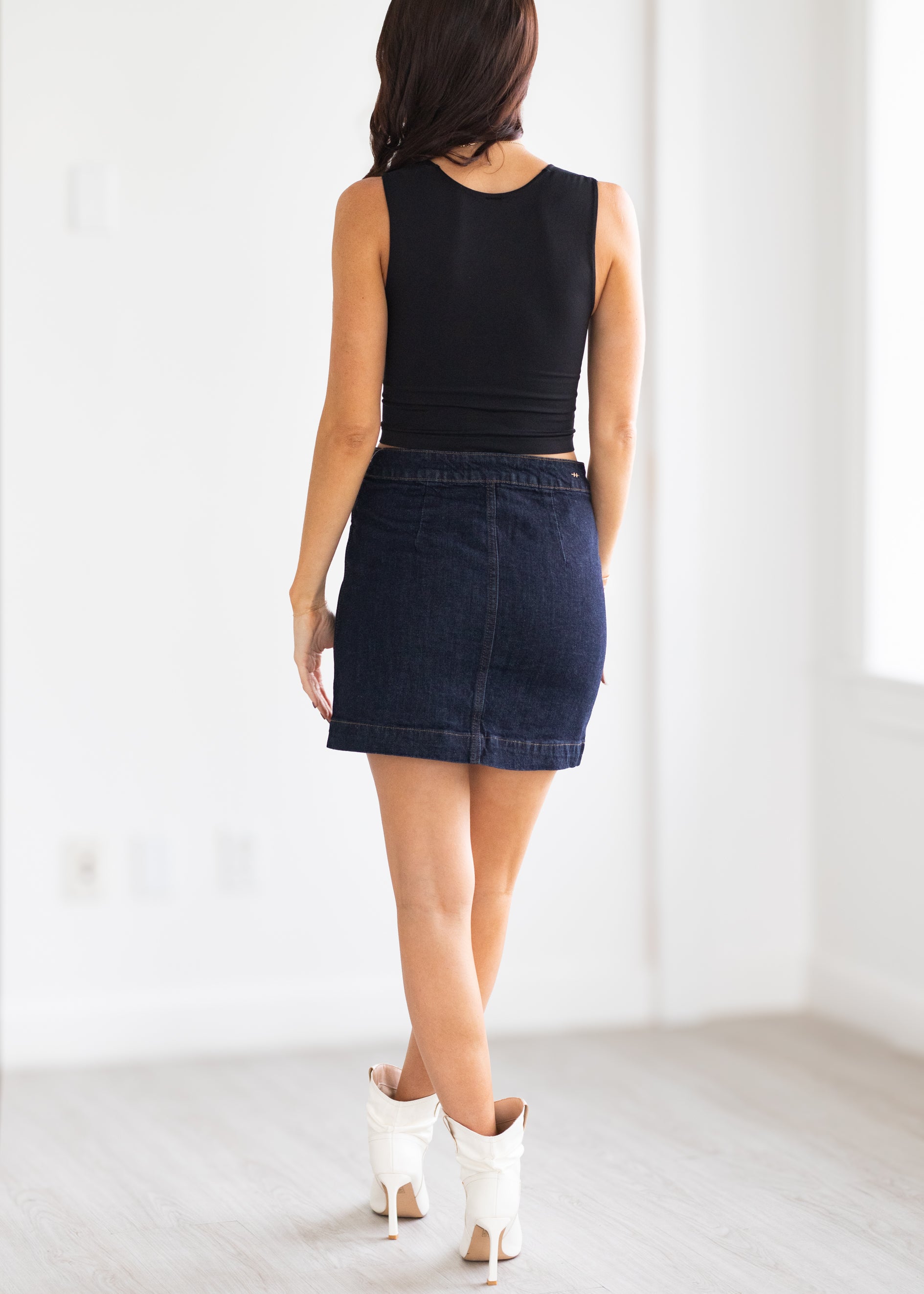Woman wearing a black tank top and dark denim skirt on a white background