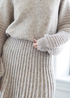 Close-up of a person wearing a soft knit sweater and matching ribbed skirt in a light oatmeal beige color, with a hand resting near the waist.