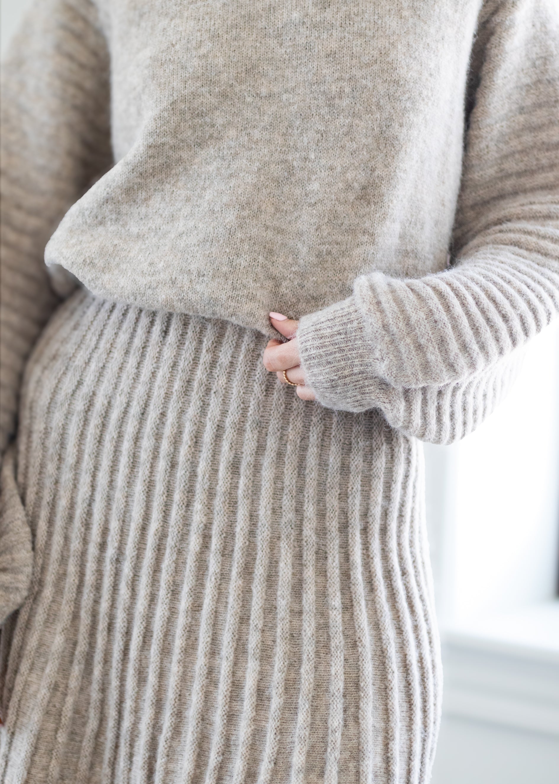Close-up of a person wearing a soft knit sweater and matching ribbed skirt in a light oatmeal beige color, with a hand resting near the waist.