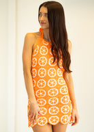 Woman wearing an orange dress with white patterns on a plain background