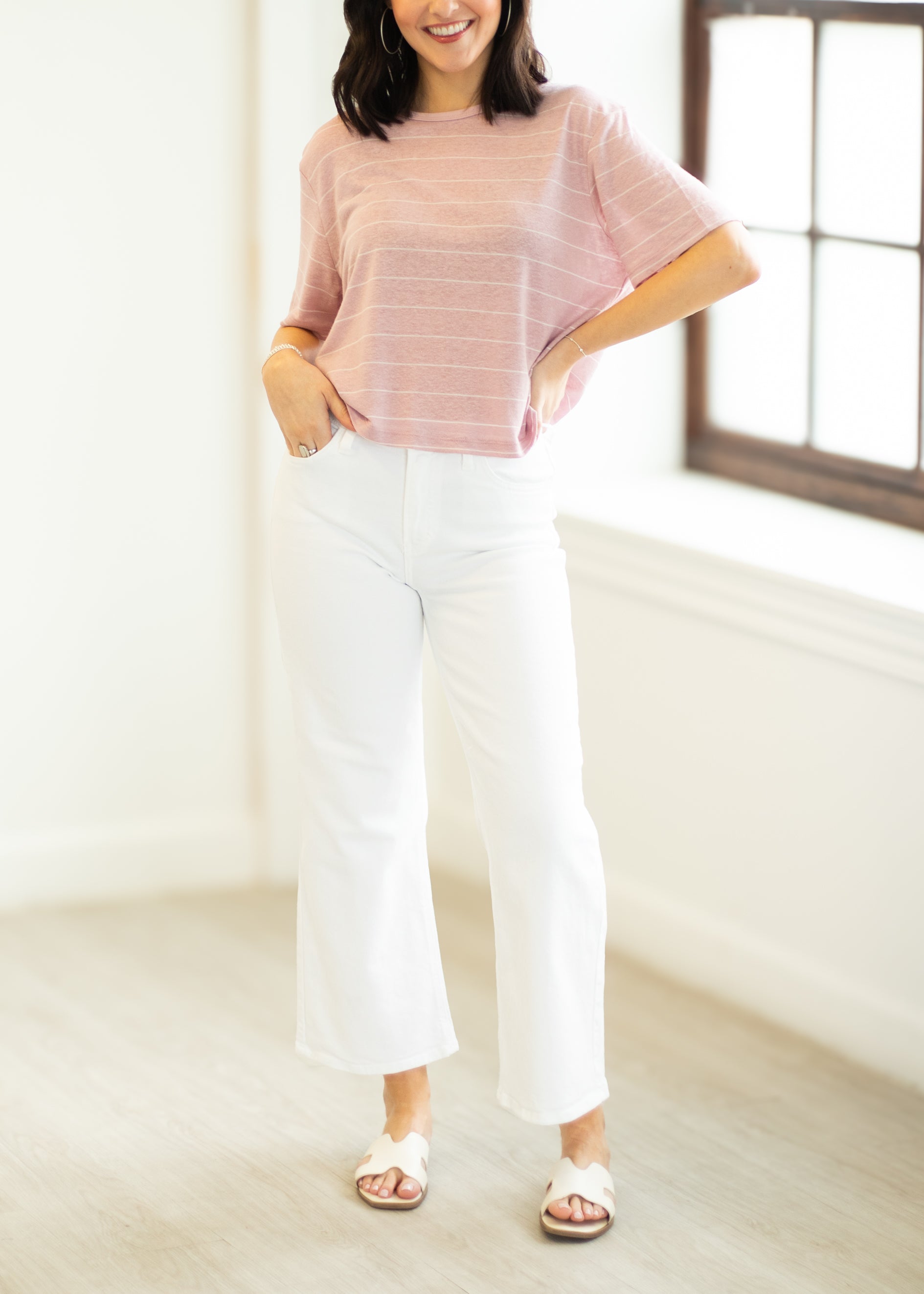 Woman wearing a pink striped shirt and white pants in a bright room.