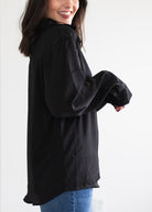 Woman wearing a black long-sleeve shirt with rolled-up sleeves against a white background