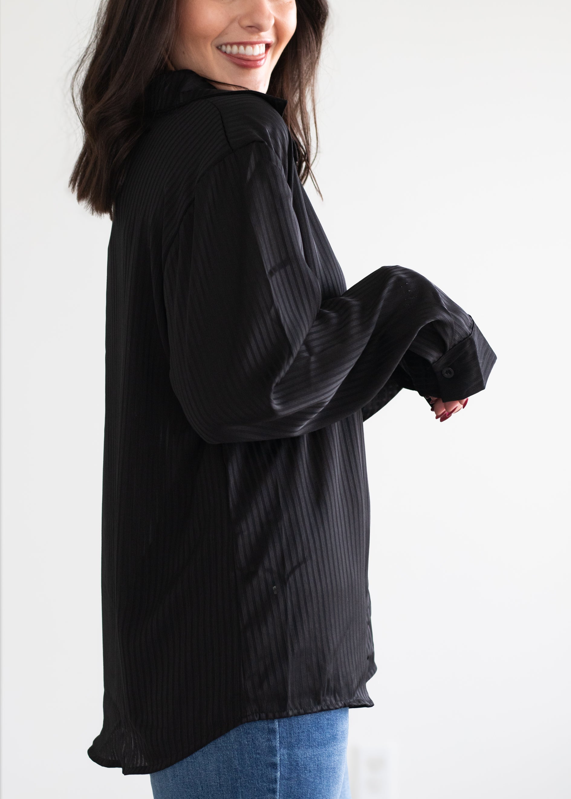 Woman wearing a black long-sleeve shirt with rolled-up sleeves against a white background