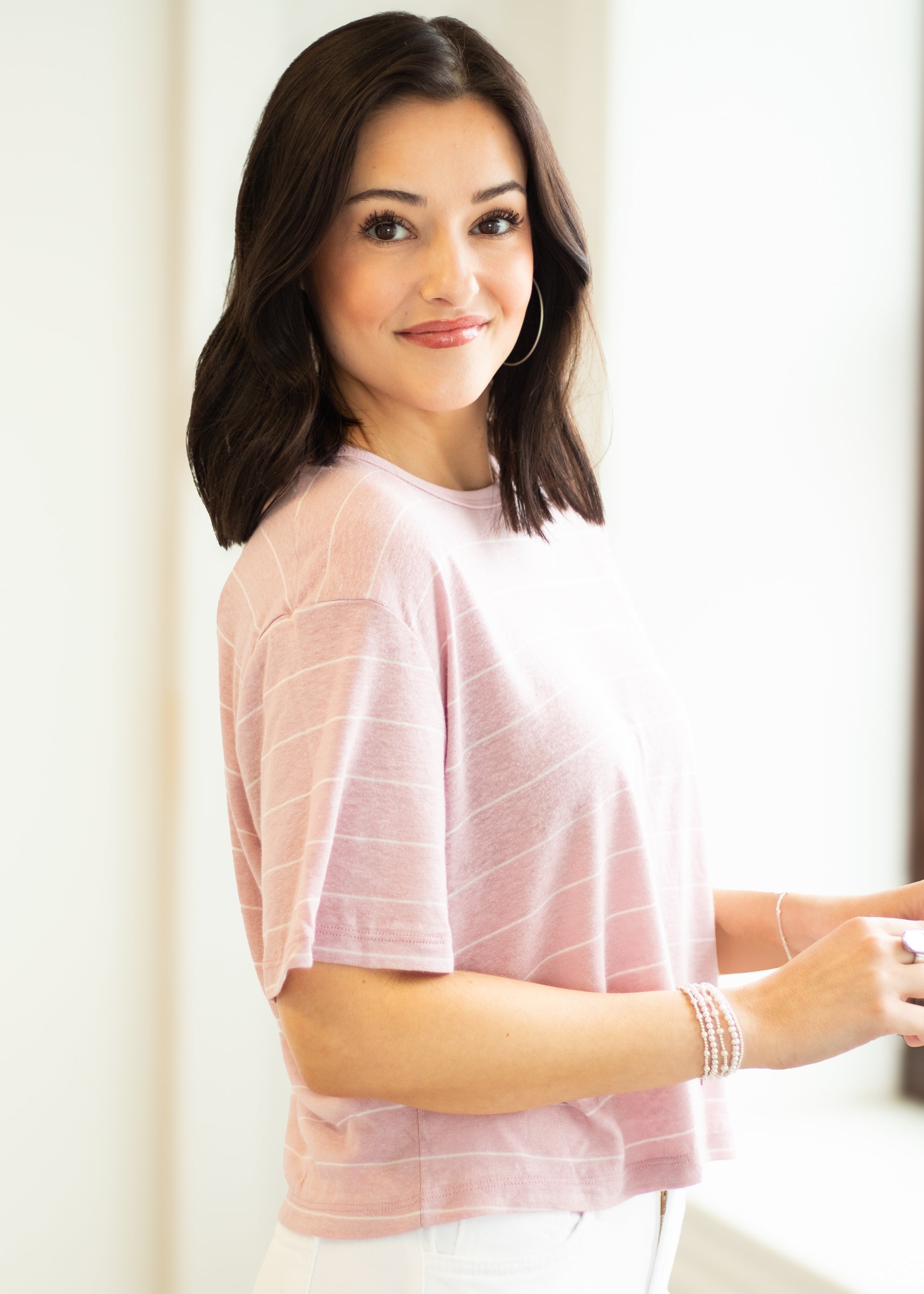 Woman wearing a light pink top with thin stripes against a white background