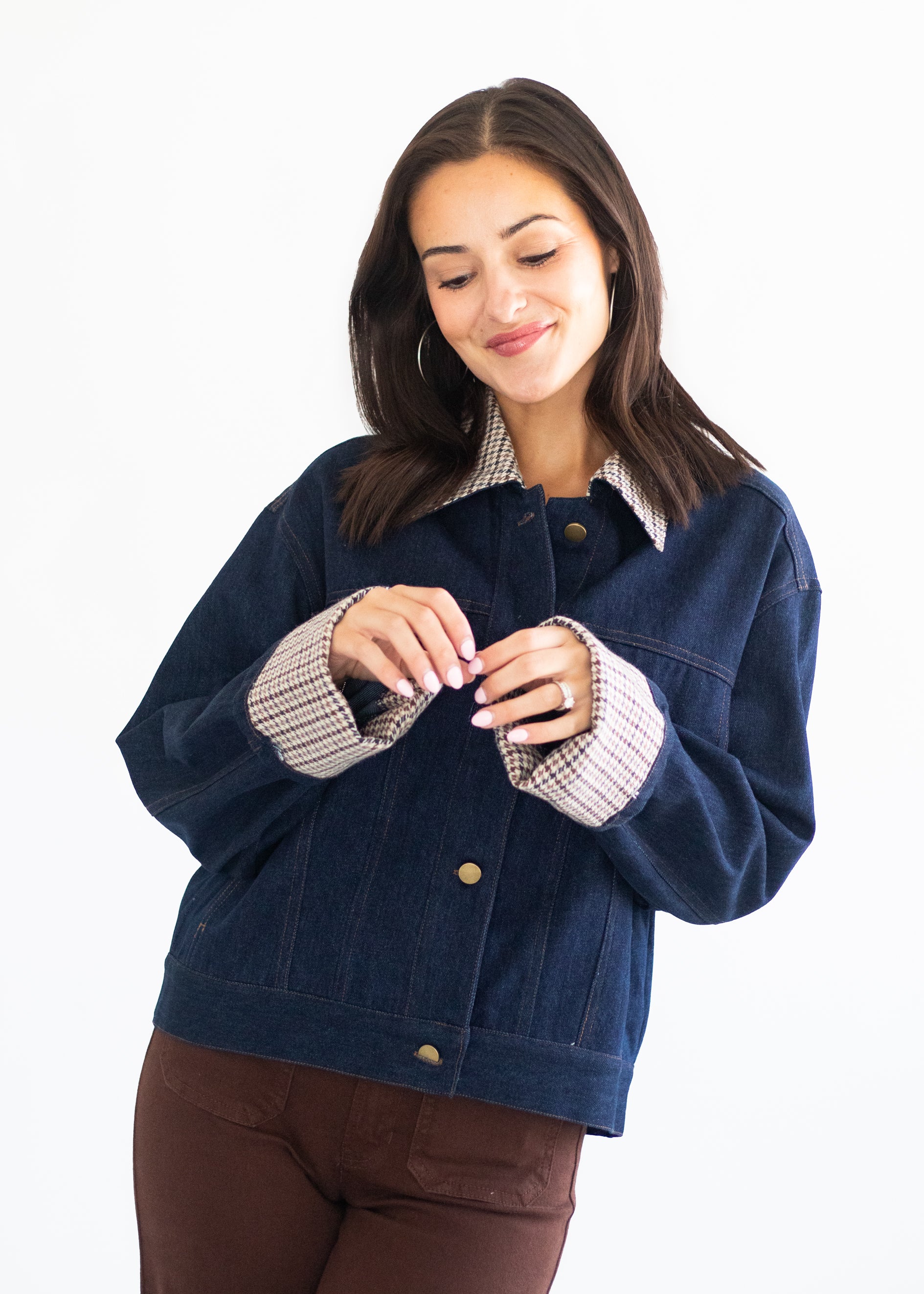 A woman wearing a dark blue denim jacket with a beige and white checkered inner collar and cuffs, paired with brown pants, against a plain white background.