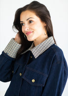 A woman wearing a dark blue denim jacket with a contrasting beige and black houndstooth patterned collar, posed against a clean white background.