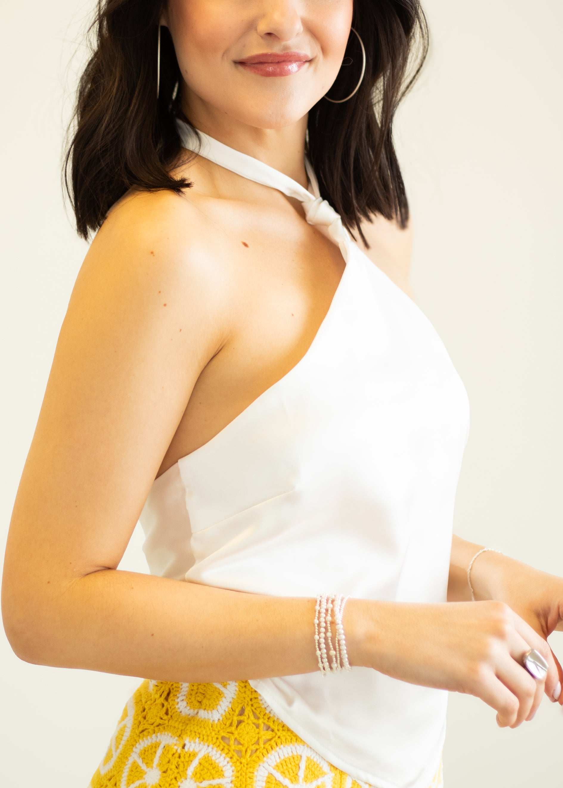 Woman wearing a white halter top and yellow patterned pants on a plain background