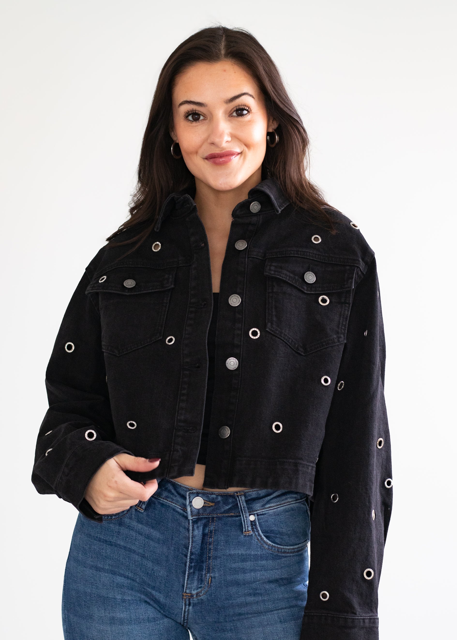 Woman wearing a black denim jacket with silver buttons on a plain background