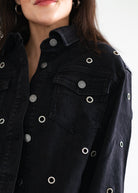 Black denim jacket with silver buttons and eyelets worn by a person.