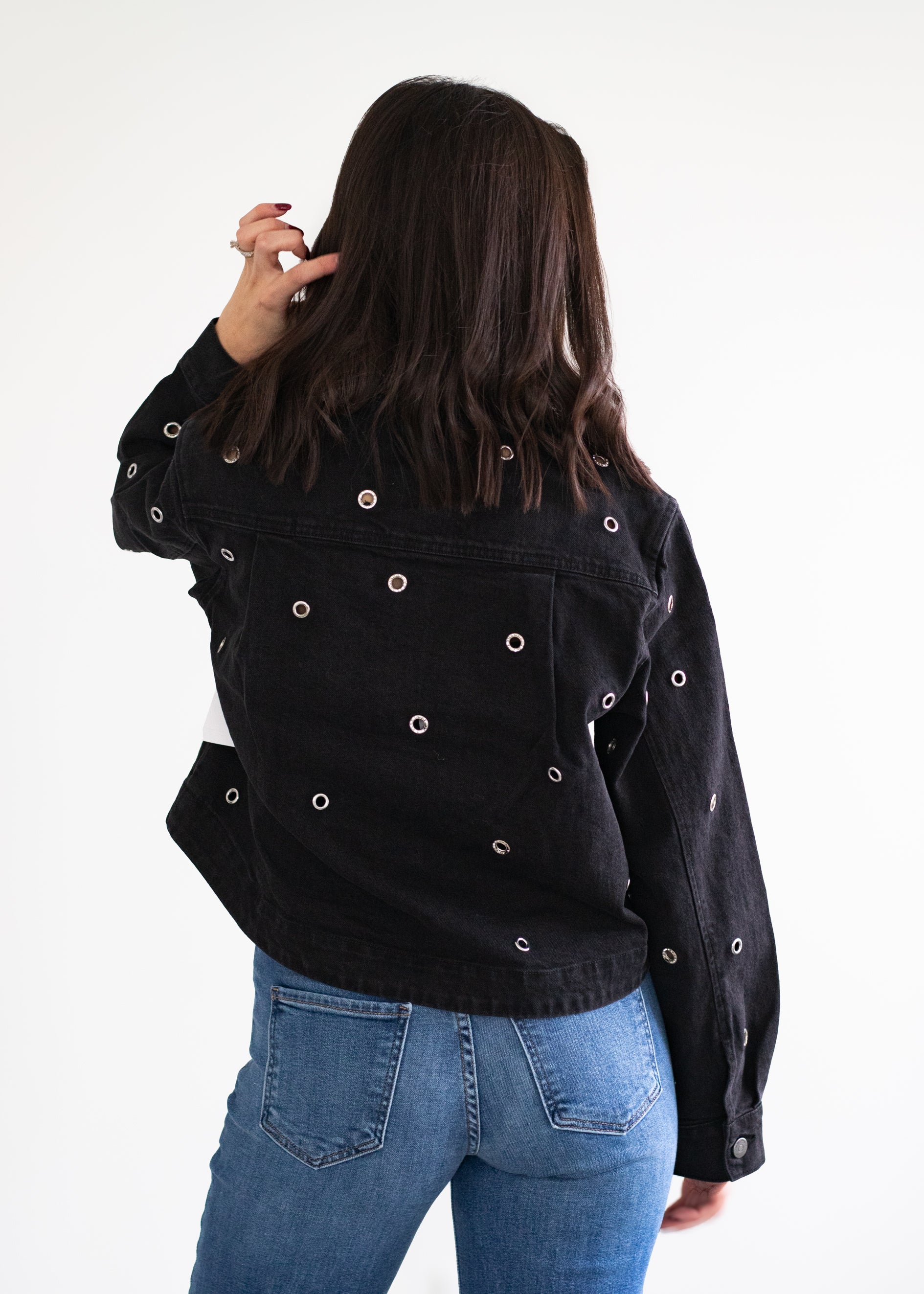 Person wearing a black jacket with button details and blue jeans on a white background