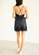 Woman wearing a black lace nightgown with white polka dots on a plain background
