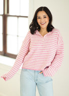 Woman wearing a pink striped sweater and light blue jeans indoors.