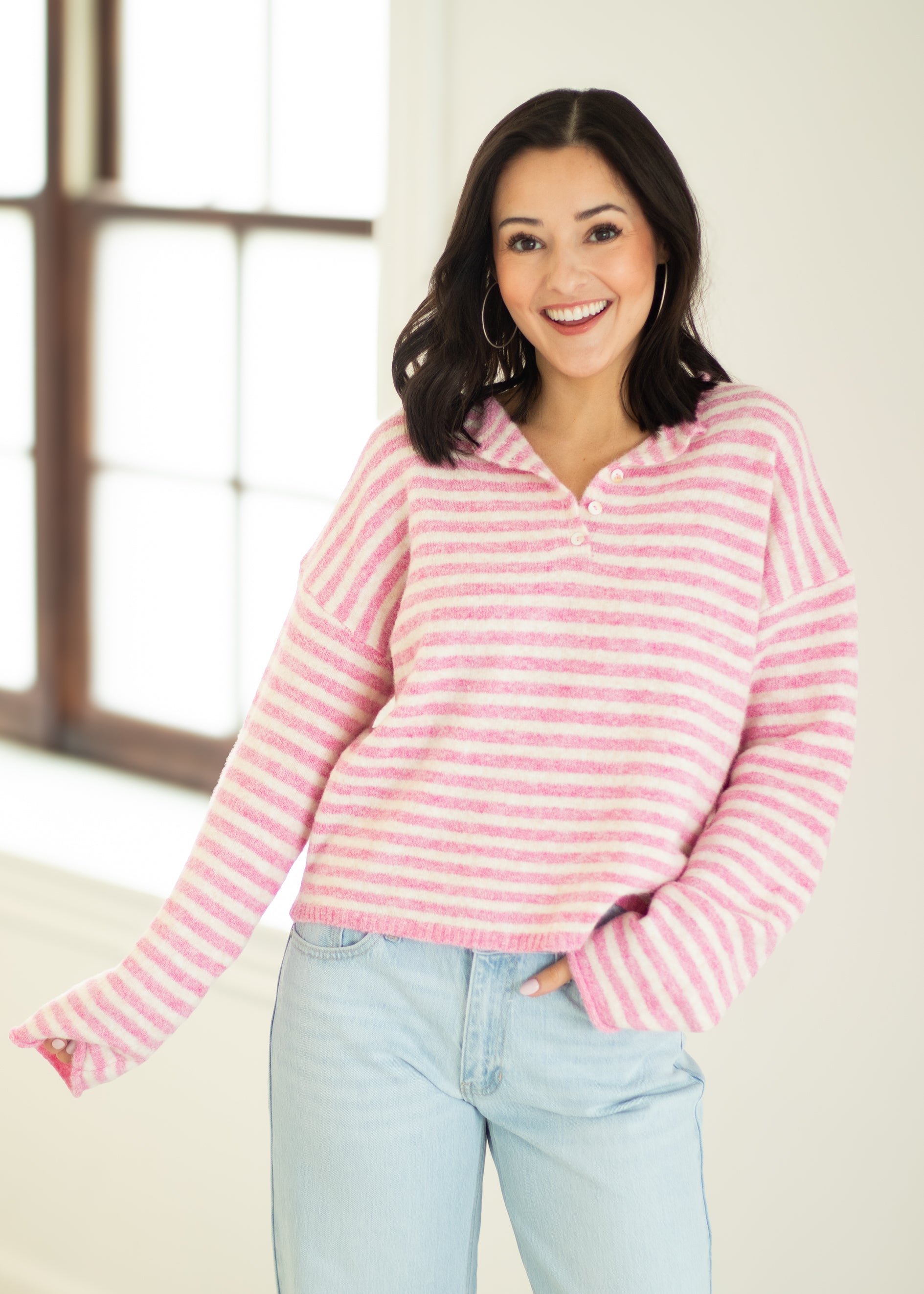 Woman wearing a pink striped sweater and light blue jeans indoors.