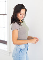 A woman wearing a short-sleeve crewneck t-shirt with thin gray and white horizontal stripes, paired with light blue jeans, standing in a brightly lit room.