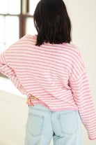 Person wearing a pink and white striped sweater and light blue jeans indoors.