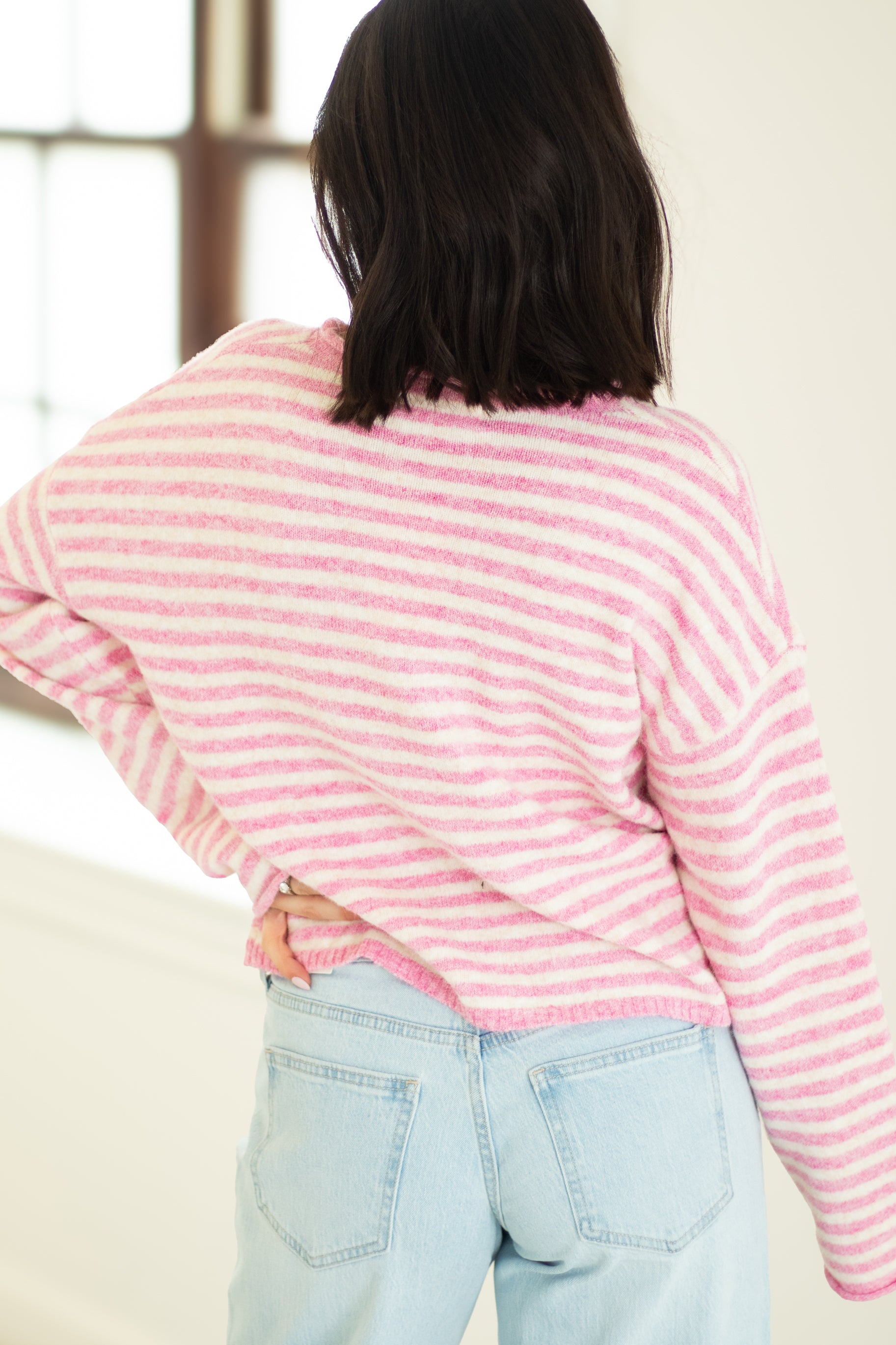 Person wearing a pink and white striped sweater and light blue jeans indoors.