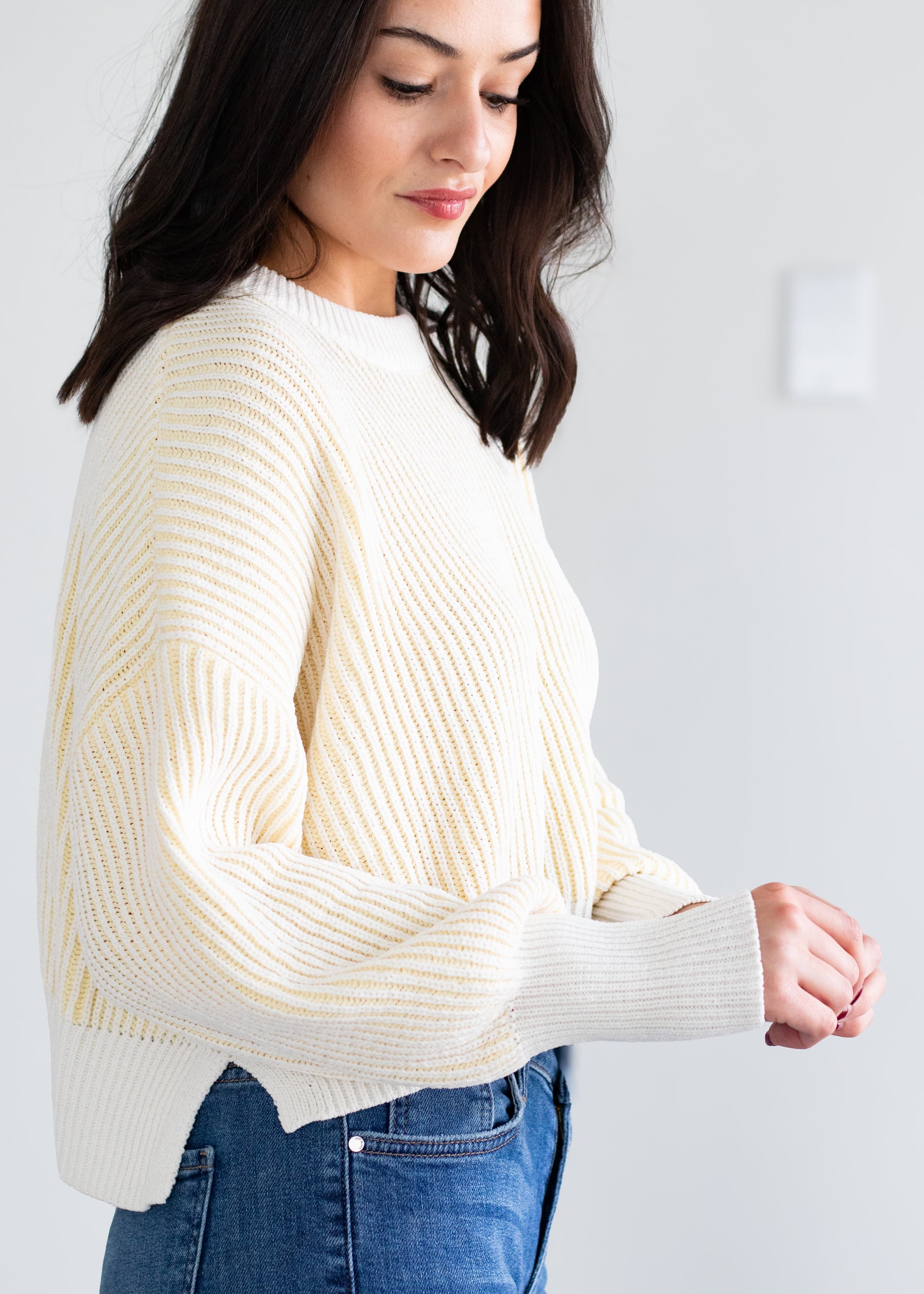 Woman wearing a cream sweater and blue jeans against a white background