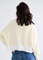 Person wearing a cream ribbed sweater and blue jeans on a white background