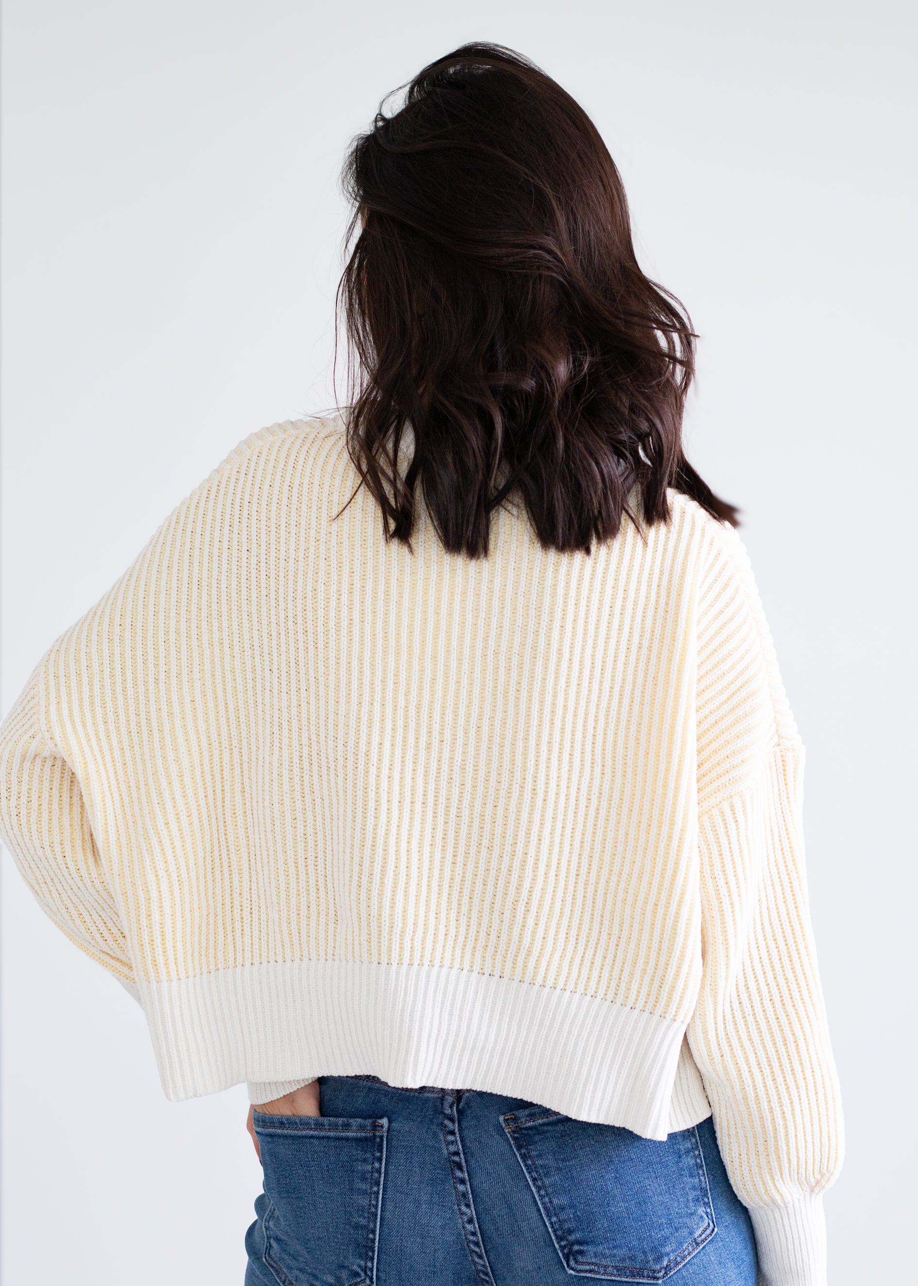 Person wearing a cream ribbed sweater and blue jeans on a white background