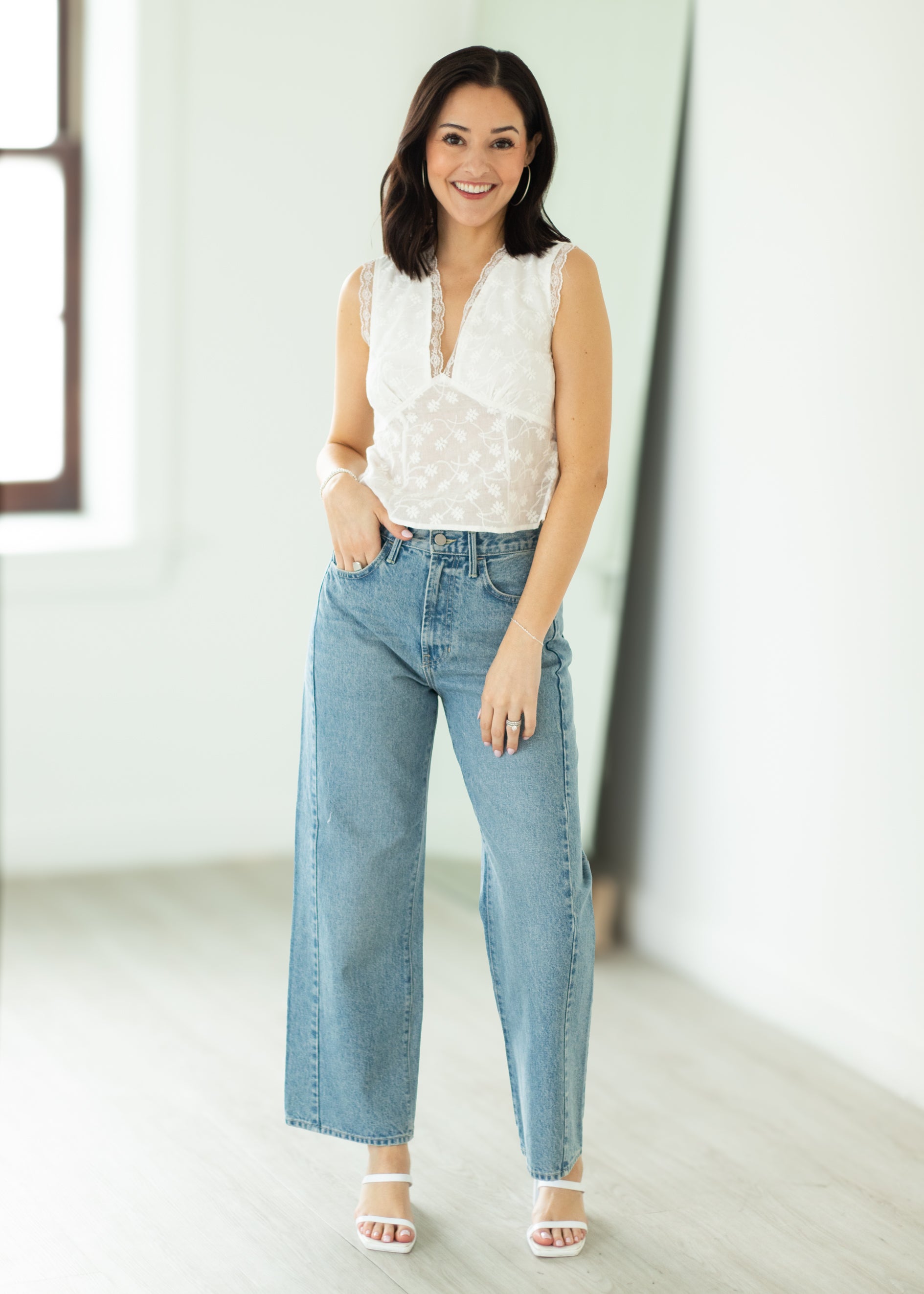 Woman wearing a white blouse and light blue jeans in a bright room.