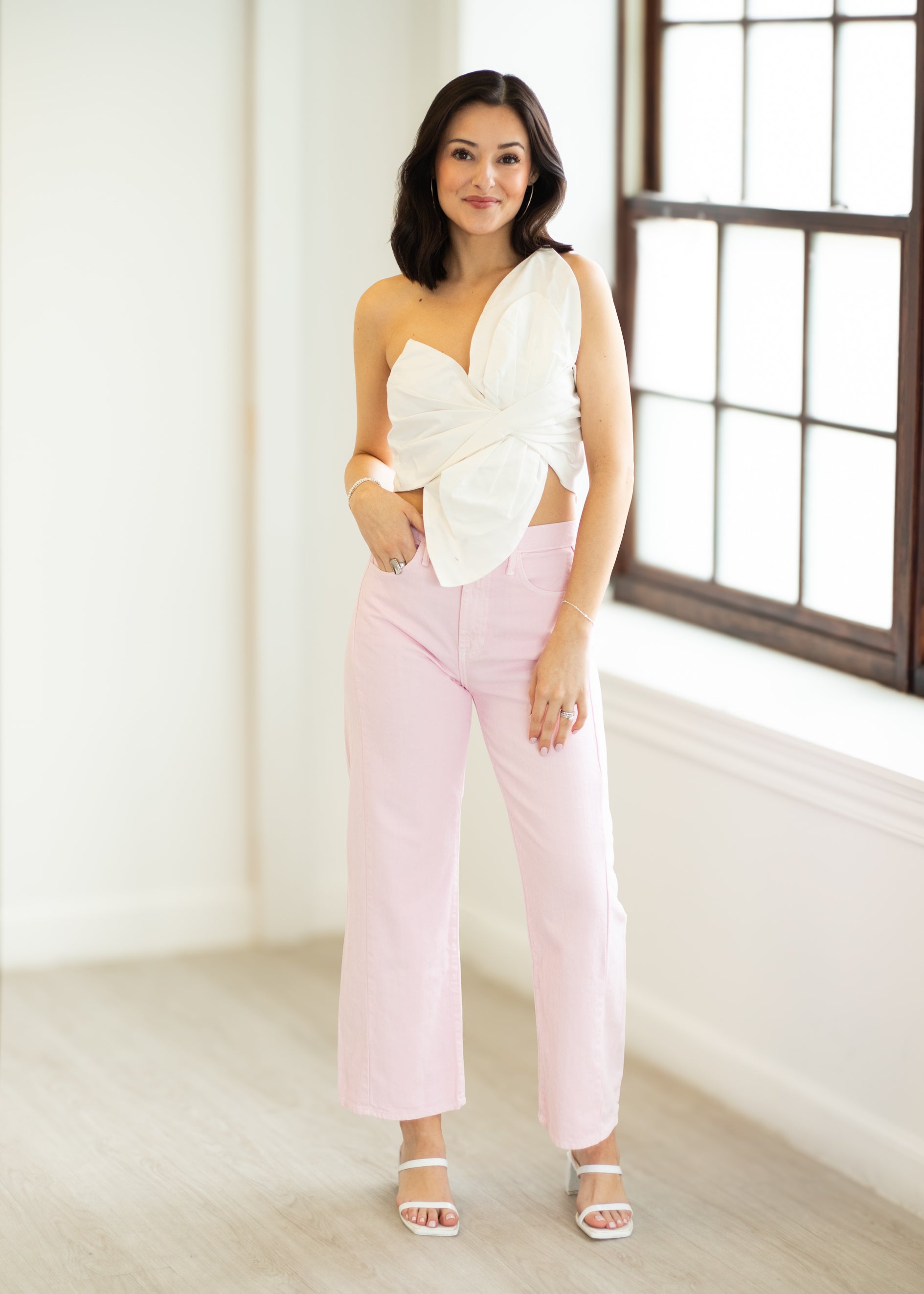 Woman wearing a white top and pink pants in a bright room.