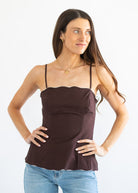 A woman modeling a dark brown spaghetti-strap camisole top with a scalloped neckline, paired with light blue jeans, against a plain white background.