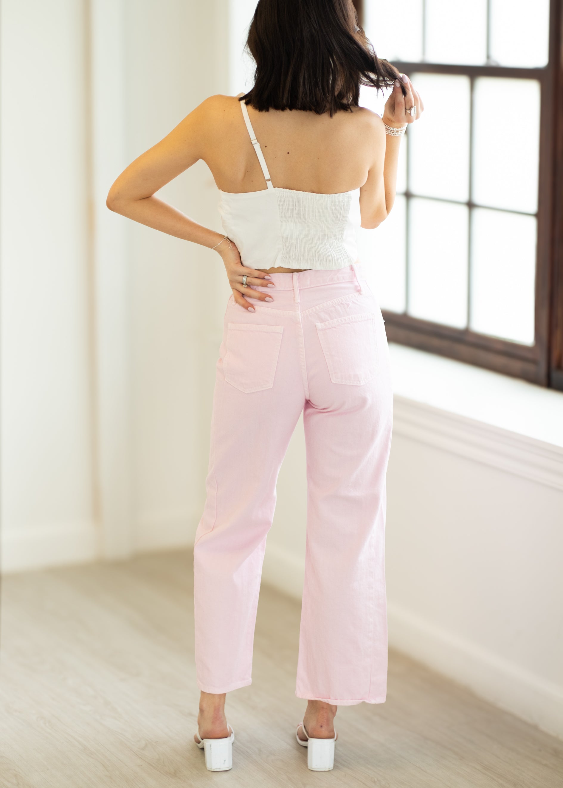 Woman wearing a white top and pink pants in a minimalistic room.
