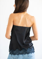 A woman shown from the back wearing a black strapless satin top with a scalloped lace hem, paired with light blue jeans, against a plain white background.