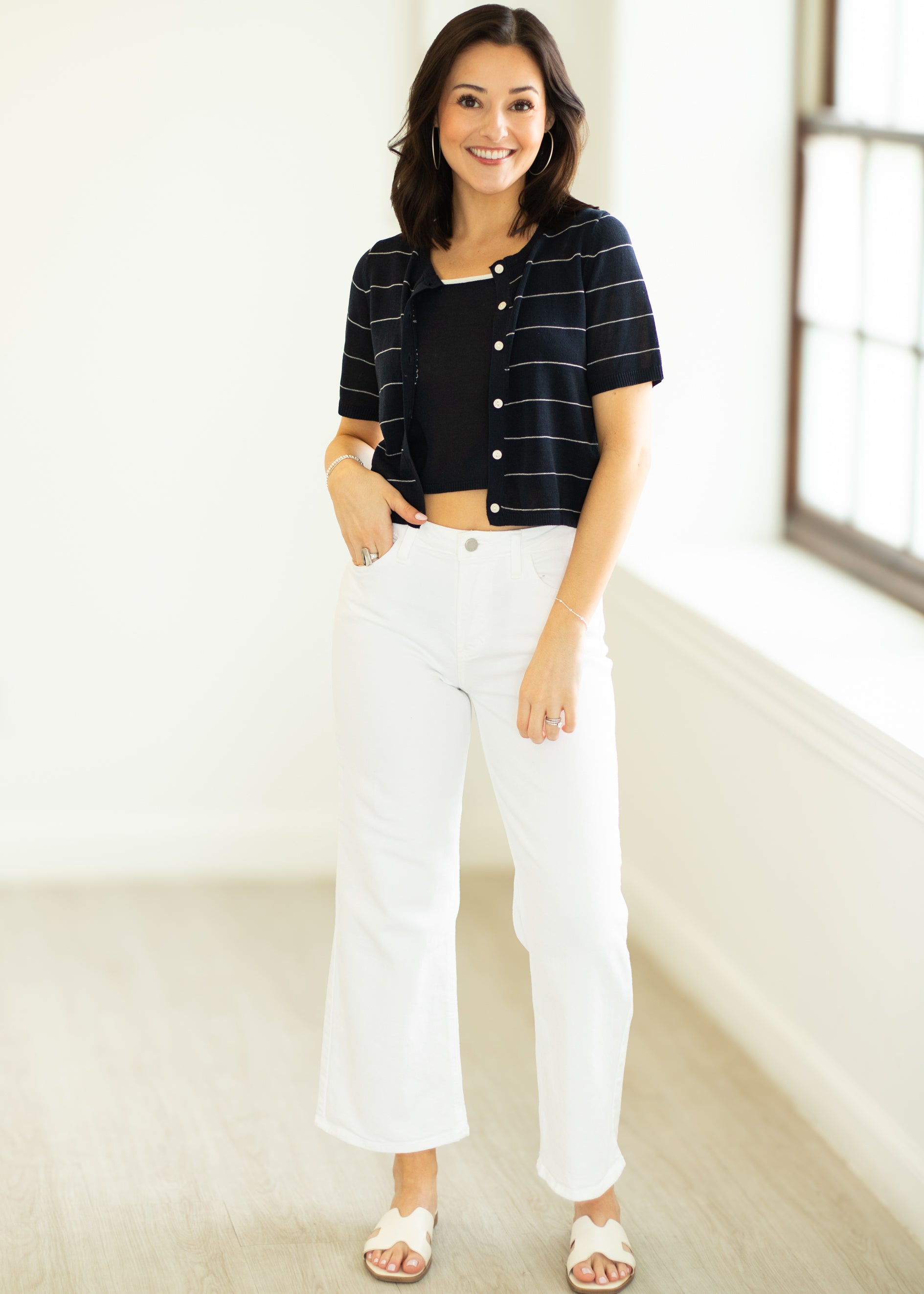 Woman wearing a striped black and white shirt and white pants indoors.