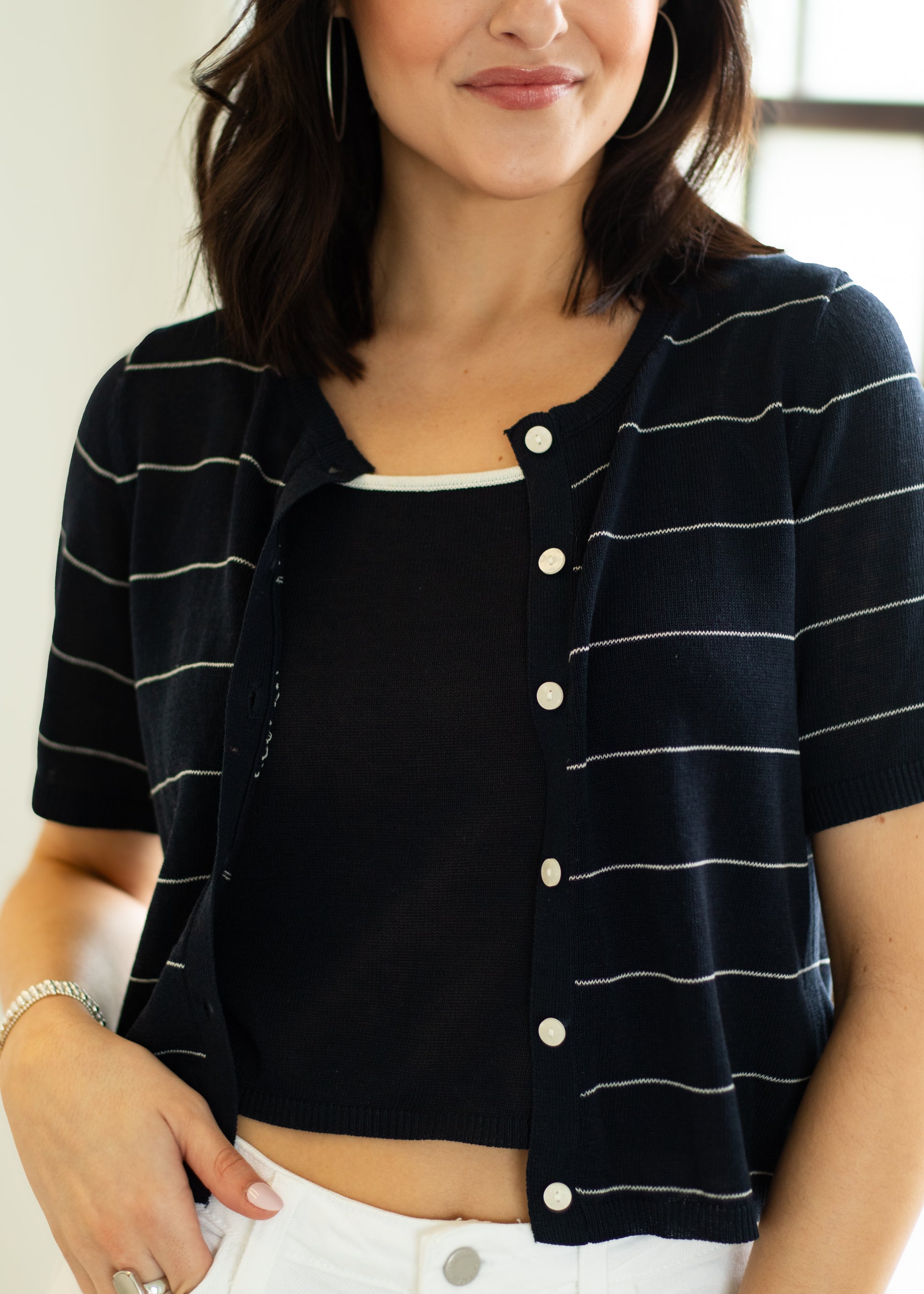 Woman wearing a black and white striped short-sleeve cardigan over a white top.