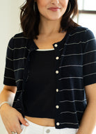 Woman wearing a black and white striped short-sleeve cardigan over a white top.