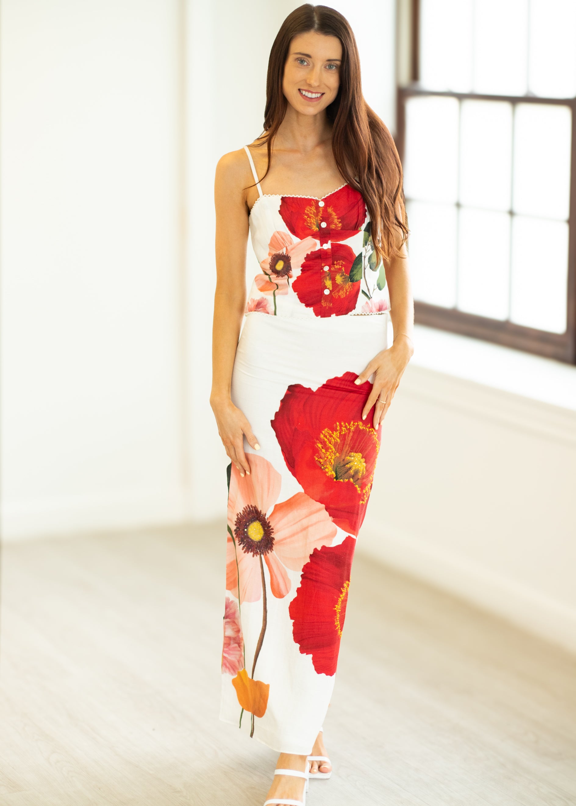 Woman wearing a floral dress with red flowers in a bright room.