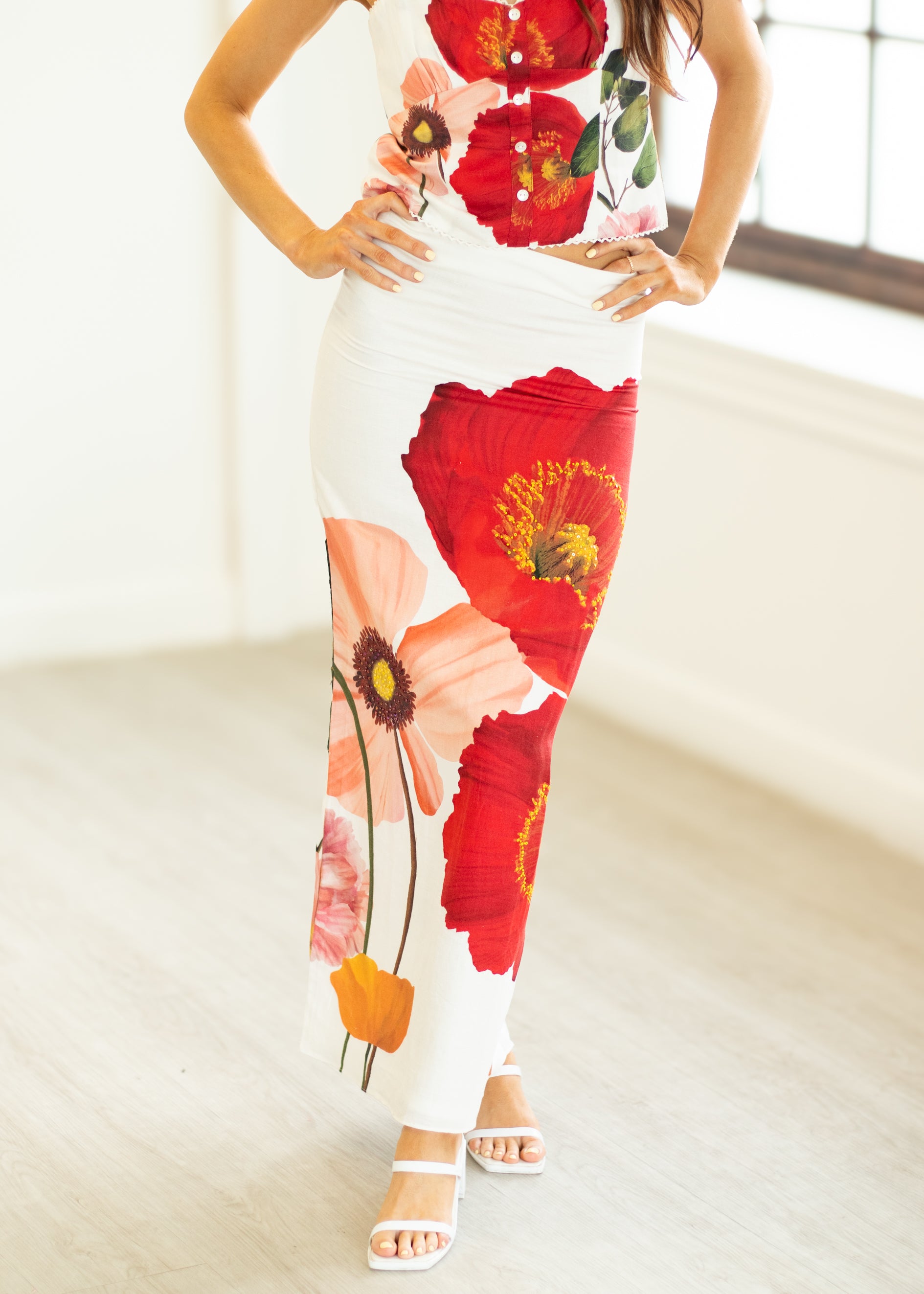 Person wearing a white dress with red floral patterns in a minimal indoor setting