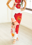Person wearing a white dress with red floral patterns in a minimal indoor setting